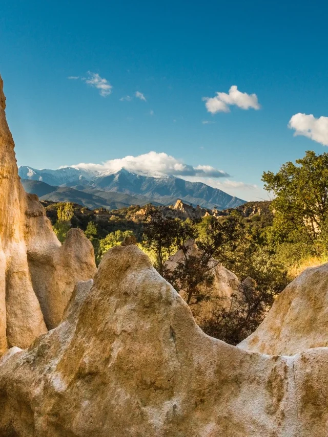 Formations rocheuses des orgues d’Ille-sur-Têt dans les Pyrénées-Orientales, avec vue sur le massif du Canigó enneigé sous un ciel bleu.