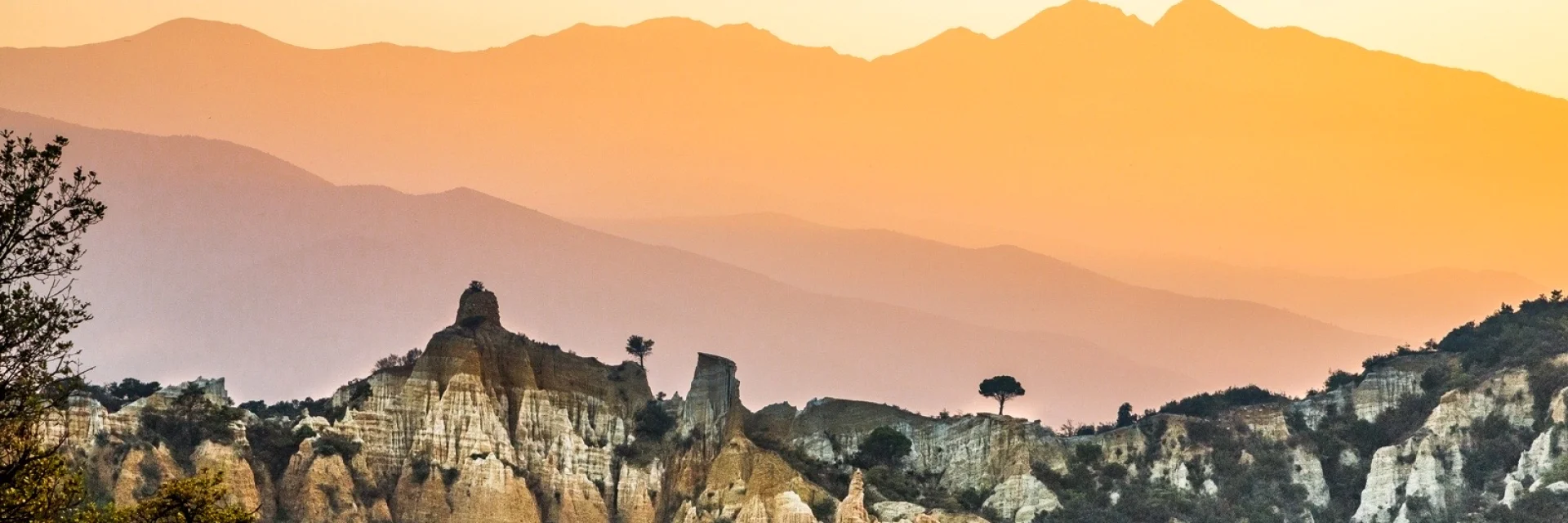 Paysage des orgues d’Ille-sur-Têt dans les Pyrénées-Orientales, formations rocheuses au premier plan avec les montagnes du Canigó en arrière-plan au coucher du soleil.