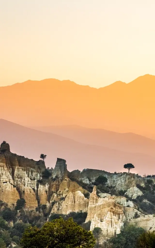 Paysage des orgues d’Ille-sur-Têt dans les Pyrénées-Orientales, formations rocheuses au premier plan avec les montagnes du Canigó en arrière-plan au coucher du soleil.