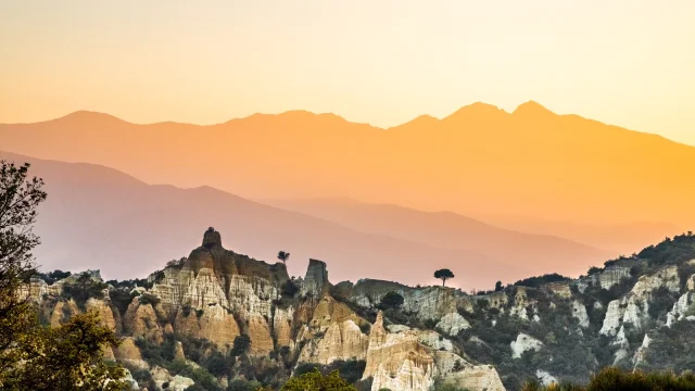 Paysage des orgues d’Ille-sur-Têt dans les Pyrénées-Orientales, formations rocheuses au premier plan avec les montagnes du Canigó en arrière-plan au coucher du soleil.