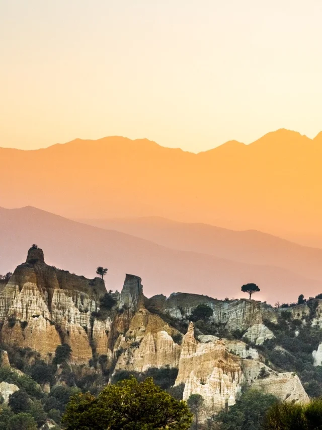 Paysage des orgues d’Ille-sur-Têt dans les Pyrénées-Orientales, formations rocheuses au premier plan avec les montagnes du Canigó en arrière-plan au coucher du soleil.