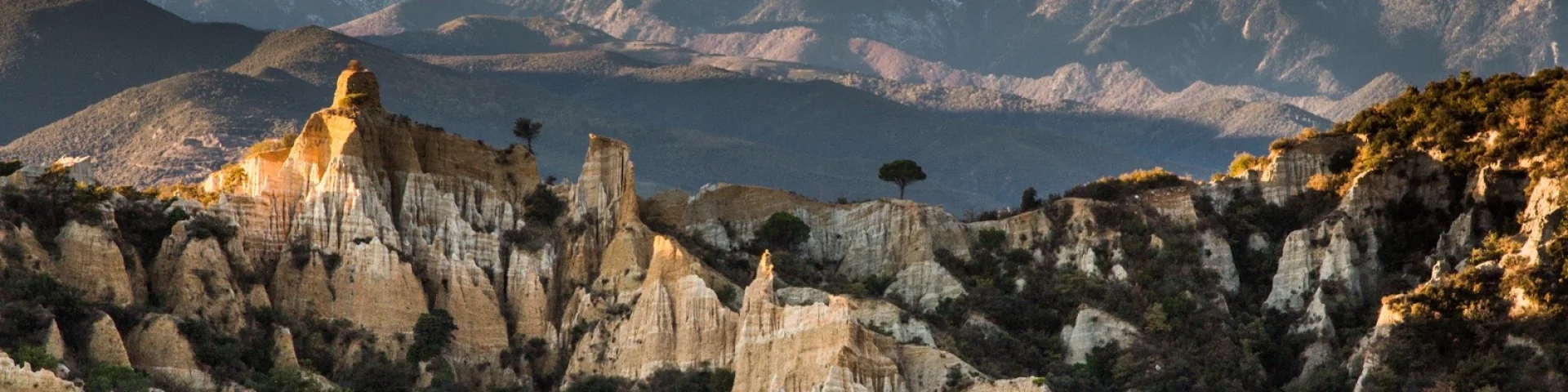 Les orgues d’Ille-sur-Têt dans les Pyrénées-Orientales, formations d’argile et de sable au premier plan, avec le massif du Canigó enneigé en arrière-plan sous un ciel bleu.