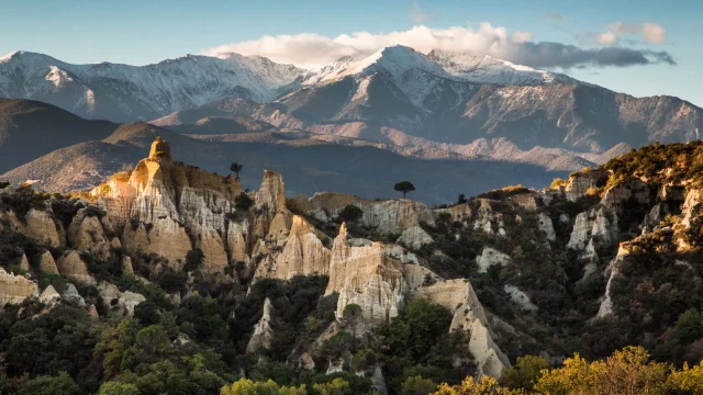 Les orgues d’Ille-sur-Têt dans les Pyrénées-Orientales, formations d’argile et de sable au premier plan, avec le massif du Canigó enneigé en arrière-plan sous un ciel bleu.