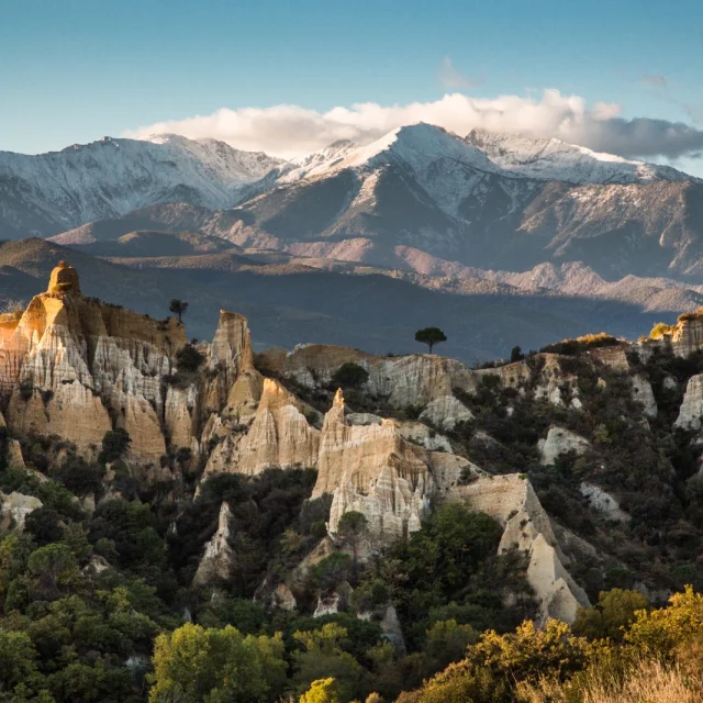 Les orgues d’Ille-sur-Têt dans les Pyrénées-Orientales, formations d’argile et de sable au premier plan, avec le massif du Canigó enneigé en arrière-plan sous un ciel bleu.