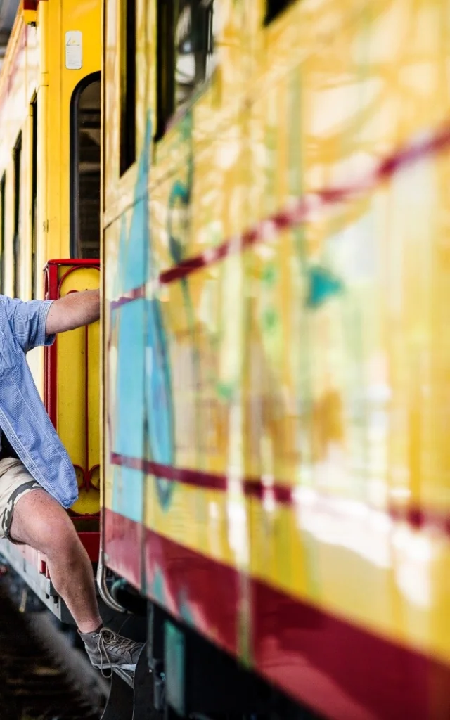 Un voyageur monte à bord du Train Jaune en gare, tenant un sac à dos, prêt à partir à la découverte des Pyrénées-Orientales.