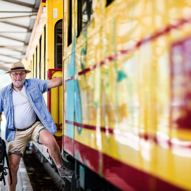 Un voyageur monte à bord du Train Jaune en gare, tenant un sac à dos, prêt à partir à la découverte des Pyrénées-Orientales.
