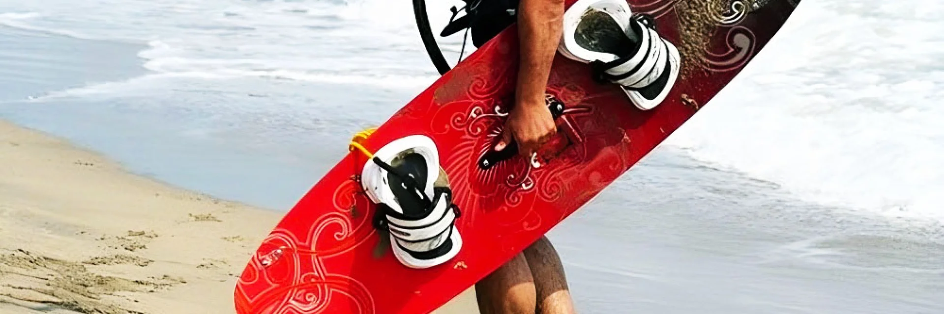 Personne marchant sur la plage en portant une planche de kitesurf rouge.