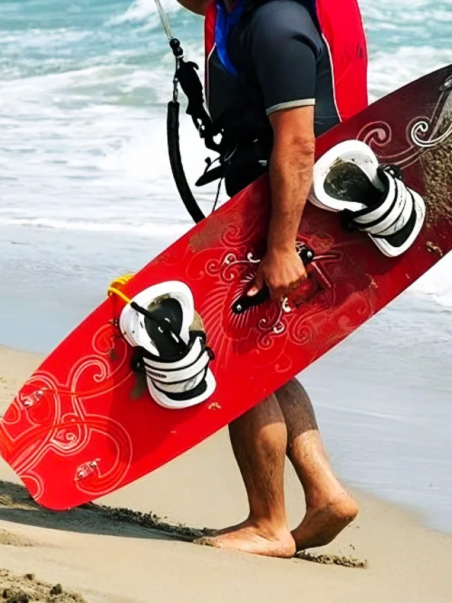 Personne marchant sur la plage en portant une planche de kitesurf rouge.