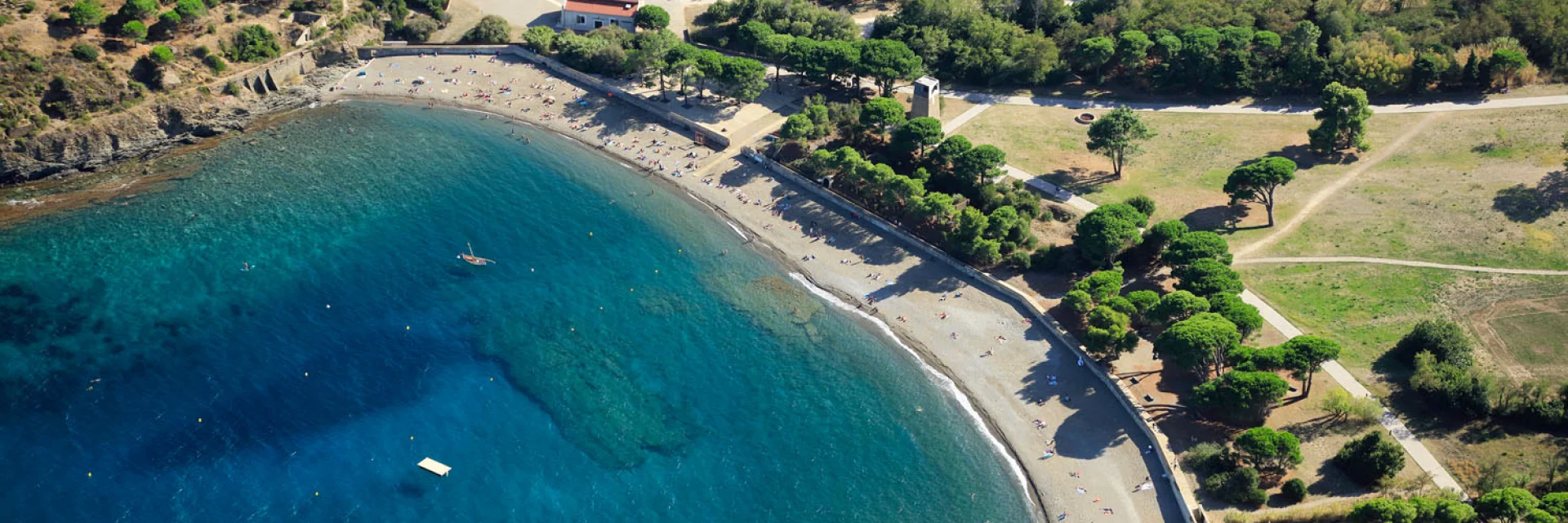 Vue aérienne de la crique de Paulilles dans les Pyrénées-Orientales, avec sa plage de galets bordée d’eaux turquoise et entourée de verdure.