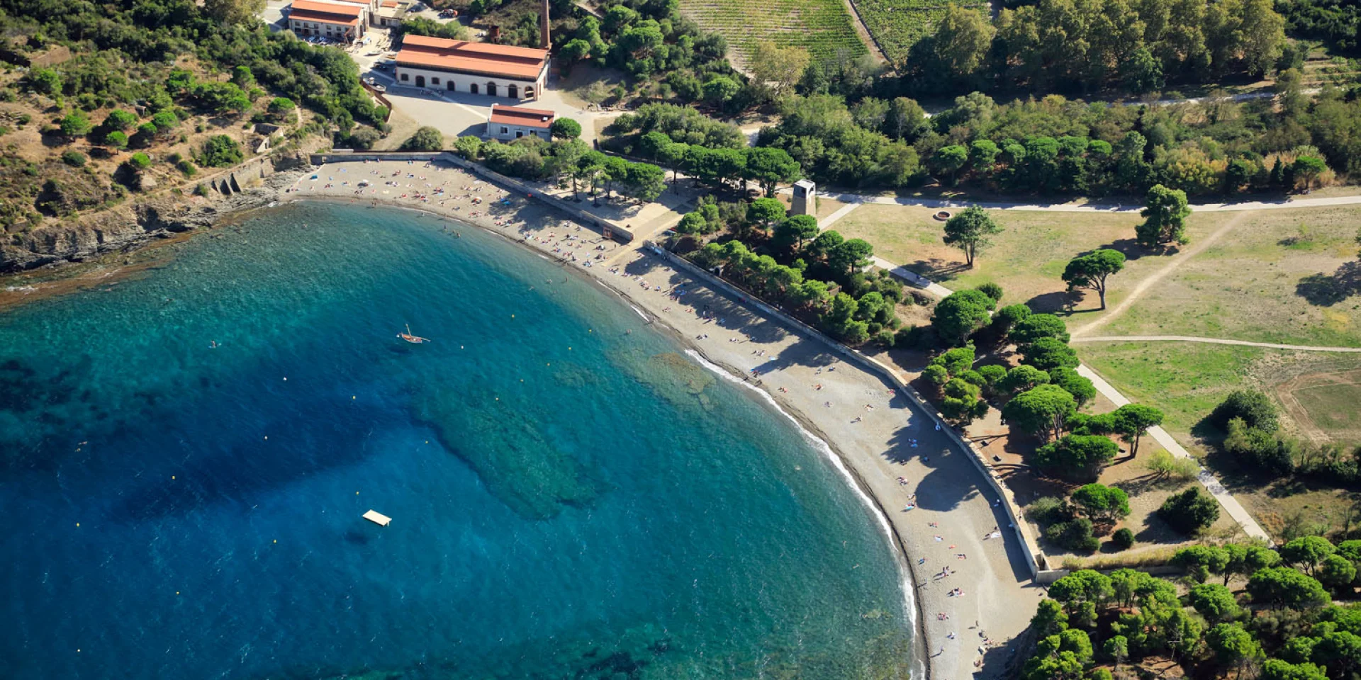 Vue aérienne de la crique de Paulilles dans les Pyrénées-Orientales, avec sa plage de galets bordée d’eaux turquoise et entourée de verdure.
