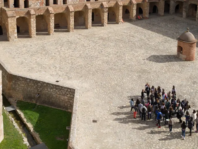 Vue aérienne de la cour intérieure de la forteresse de Salses, avec un groupe de visiteurs rassemblés près d’une échauguette en brique.