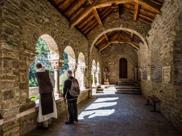 Cloître en pierre de l’abbaye Saint-Martin du Canigou avec un jardin central entouré d’arcades romanes sous un ciel bleu.