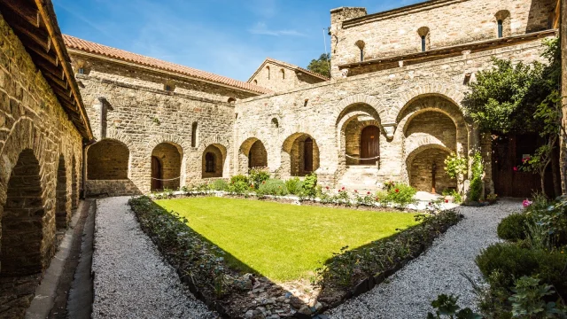 Cloître en pierre de l’abbaye Saint-Martin du Canigou avec un jardin central entouré d’arcades romanes sous un ciel bleu.
