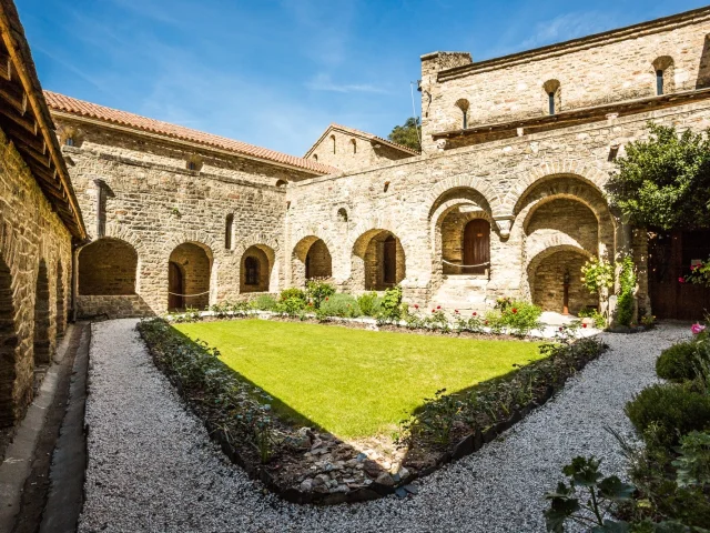 Cloître en pierre de l’abbaye Saint-Martin du Canigou avec un jardin central entouré d’arcades romanes sous un ciel bleu.