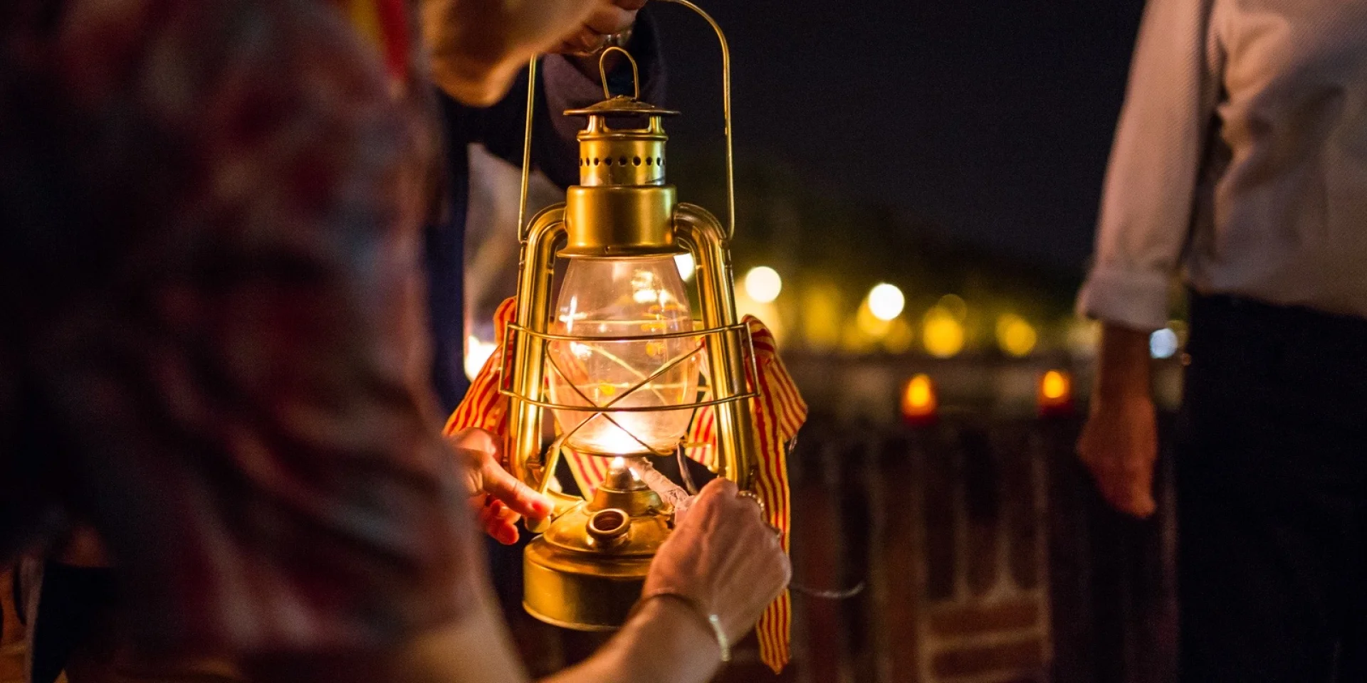 Personnes tenant une lanterne allumée ornée de rubans catalans lors de la fête de la Saint-Jean à Perpignan.