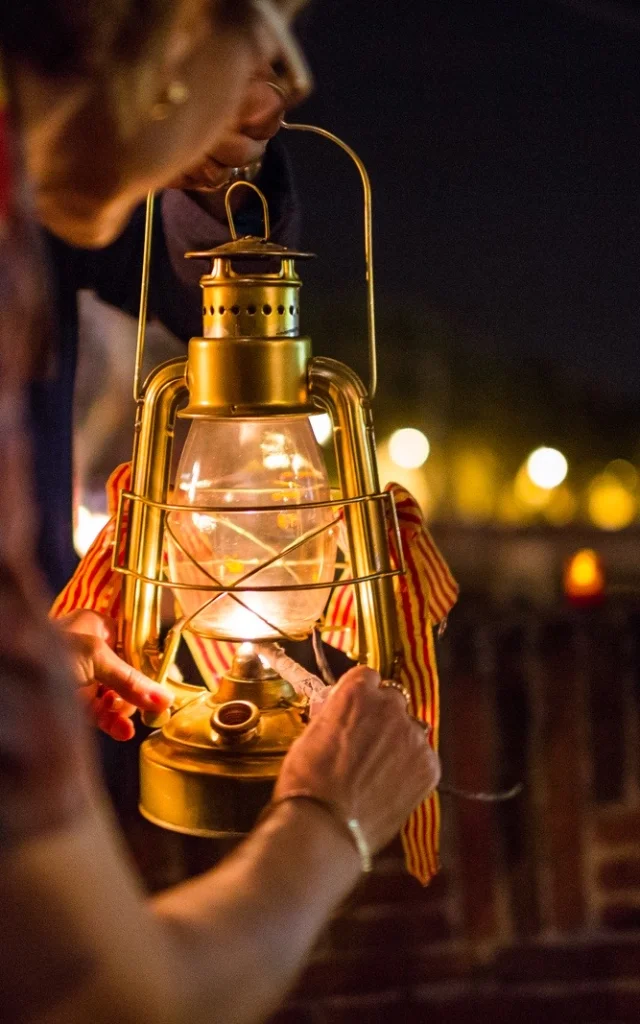 Personnes tenant une lanterne allumée ornée de rubans catalans lors de la fête de la Saint-Jean à Perpignan.