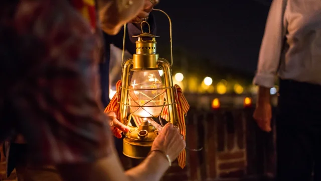 Personnes tenant une lanterne allumée ornée de rubans catalans lors de la fête de la Saint-Jean à Perpignan.