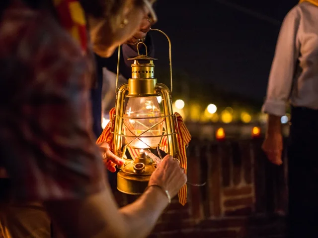 Personnes tenant une lanterne allumée ornée de rubans catalans lors de la fête de la Saint-Jean à Perpignan.