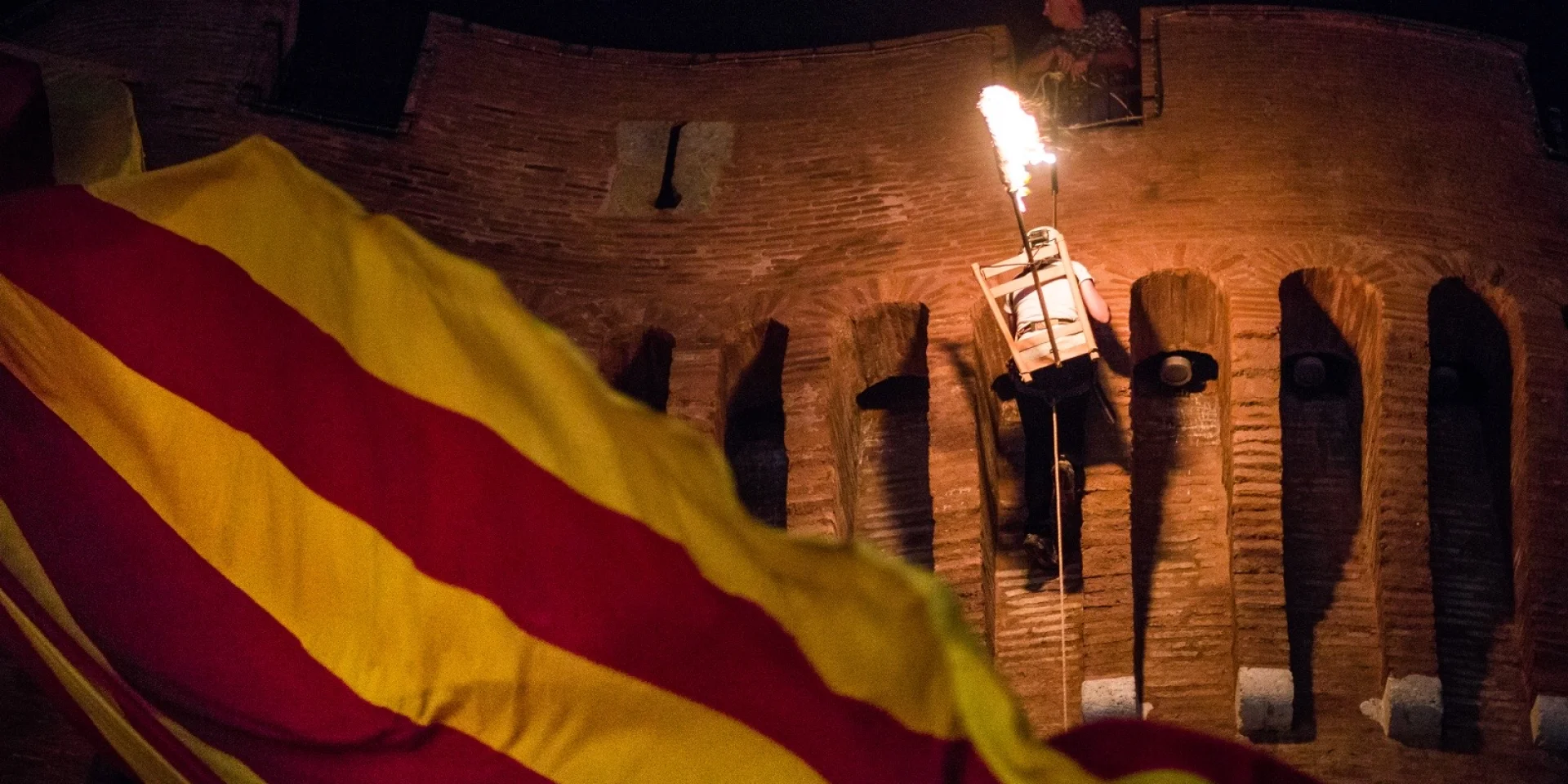 Descente de la flamme de la Saint-Jean depuis le Castillet à Perpignan, avec un drapeau catalan au premier plan.