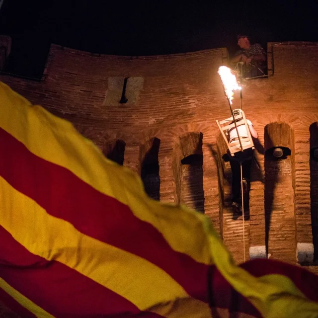 Descente de la flamme de la Saint-Jean depuis le Castillet à Perpignan, avec un drapeau catalan au premier plan.