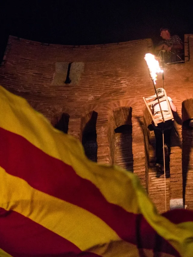 Descente de la flamme de la Saint-Jean depuis le Castillet à Perpignan, avec un drapeau catalan au premier plan.