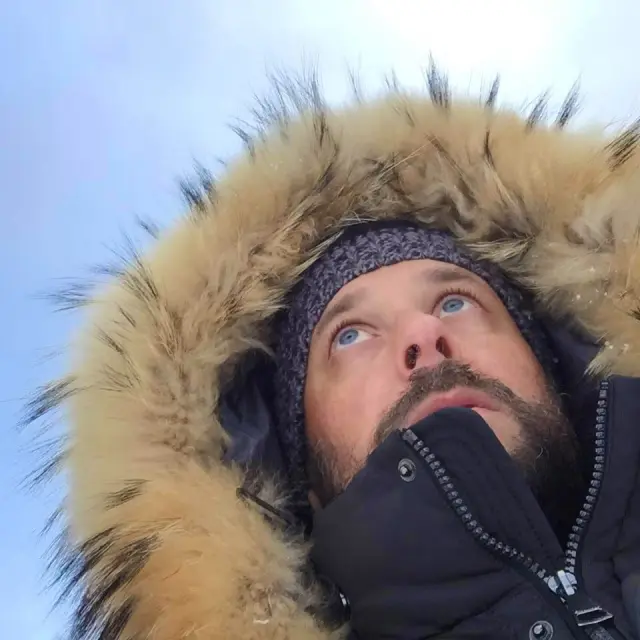 Personne vêtue d’une parka à capuche bordée de fourrure, regardant vers le ciel.