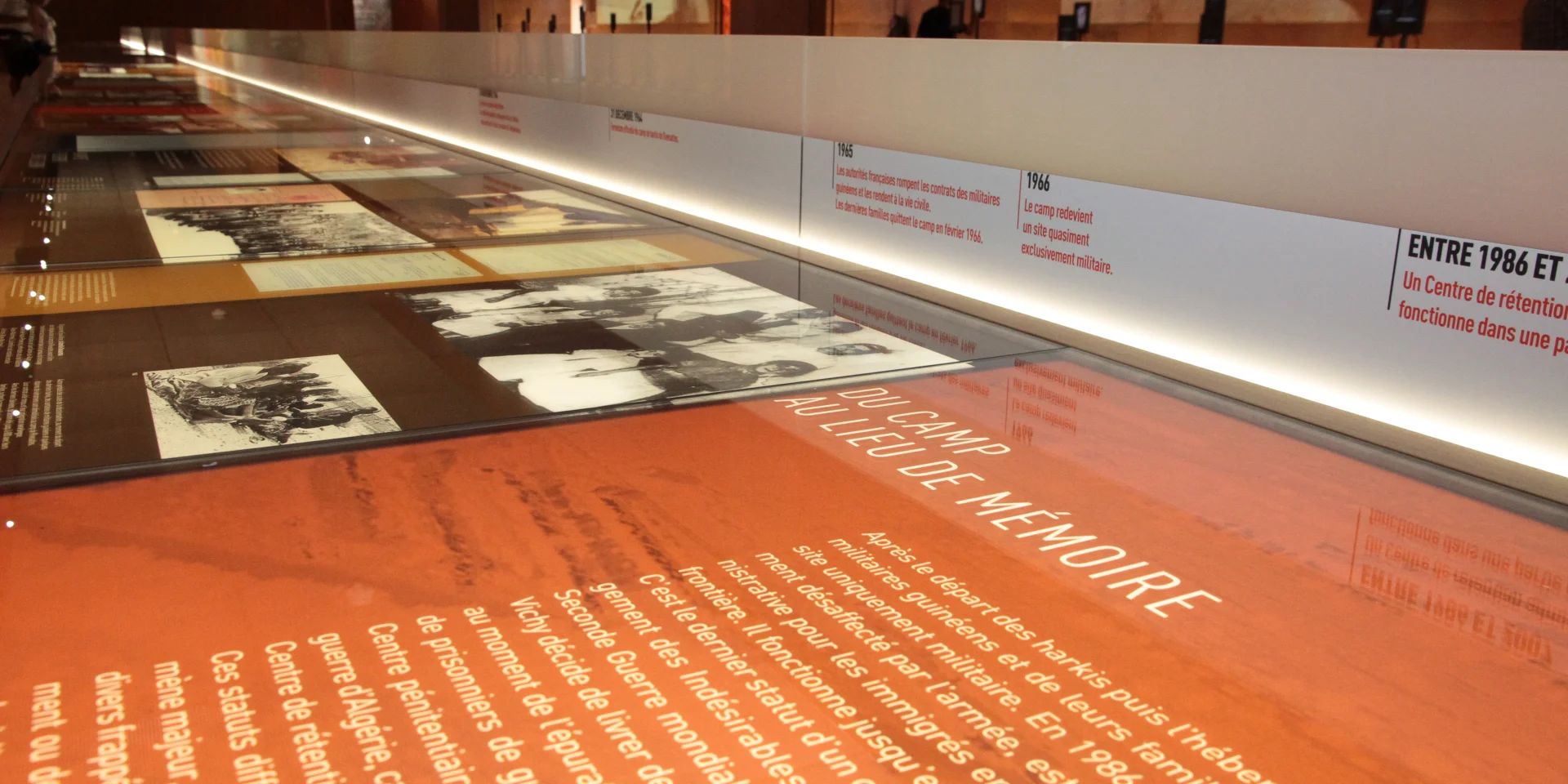 Vitrine d’exposition au Mémorial du Camp de Rivesaltes présentant des textes, des photos d’archives et une frise chronologique retraçant l’histoire du camp.