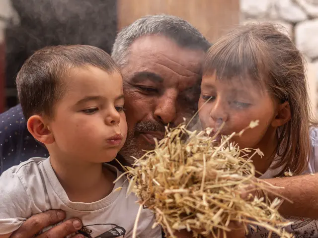 Un homme et deux enfants soufflent sur un nid de paille pour allumer un feu lors d’un atelier préhistorique à Tautavel.