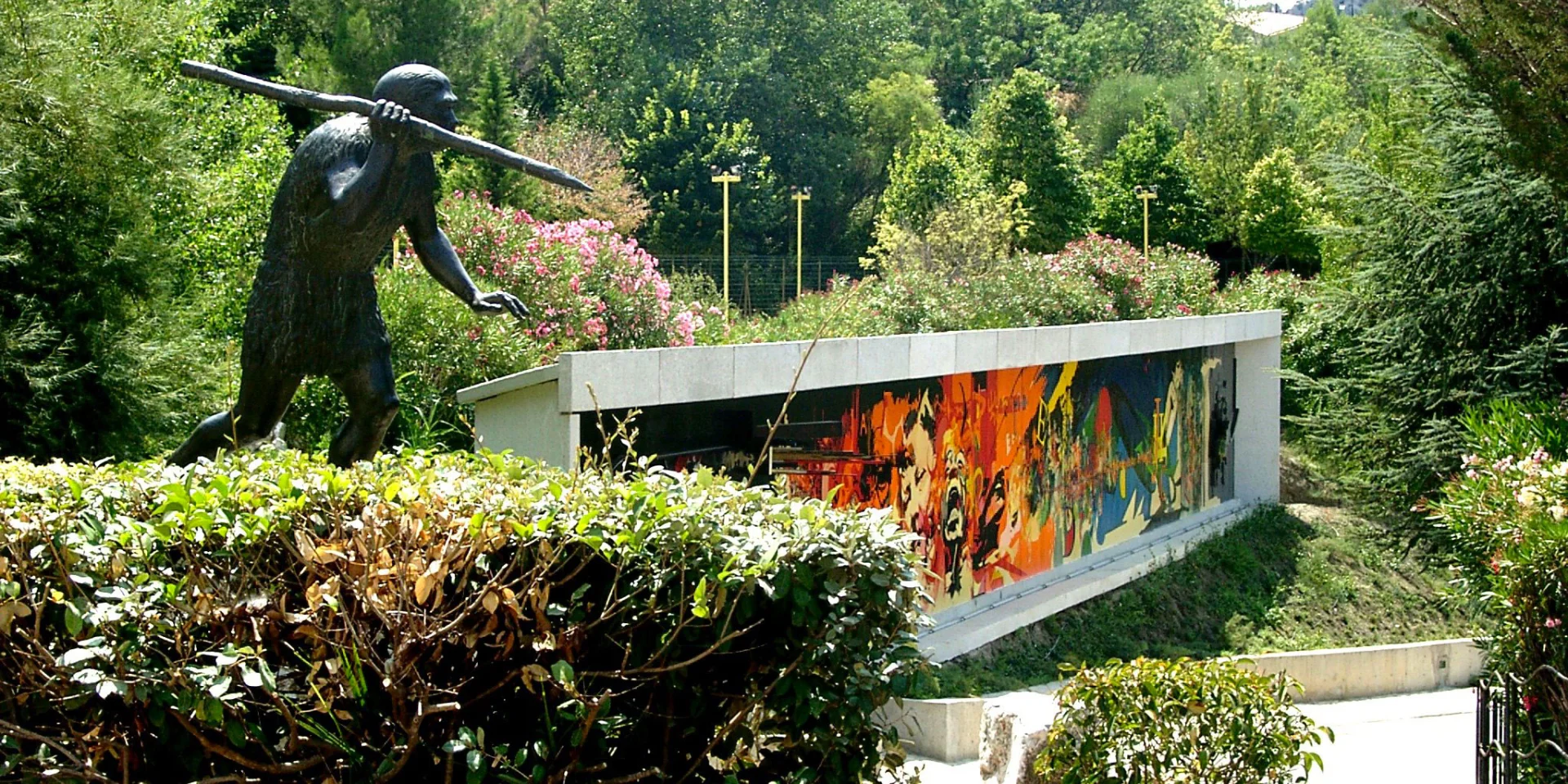 Statue préhistorique et façade colorée du musée de Préhistoire de Tautavel entourées de verdure.
