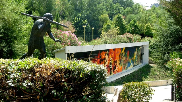 Statue préhistorique et façade colorée du musée de Préhistoire de Tautavel entourées de verdure.