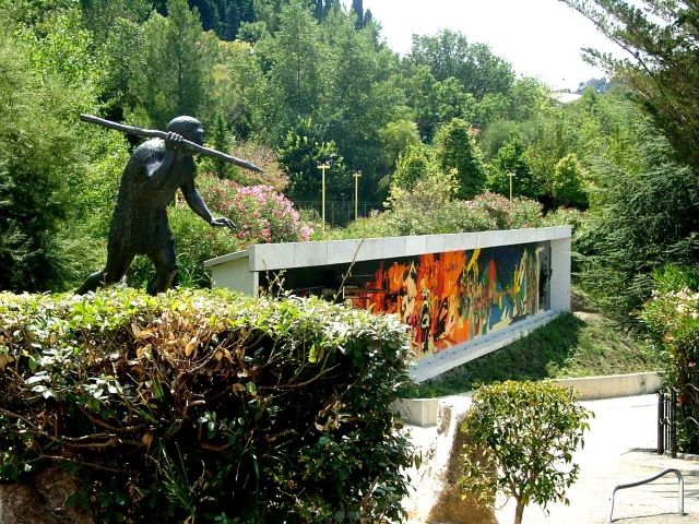 Statue préhistorique et façade colorée du musée de Préhistoire de Tautavel entourées de verdure.