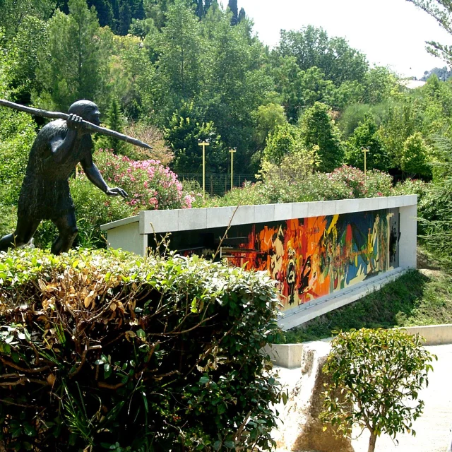 Statue préhistorique et façade colorée du musée de Préhistoire de Tautavel entourées de verdure.