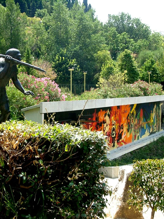 Statue préhistorique et façade colorée du musée de Préhistoire de Tautavel entourées de verdure.
