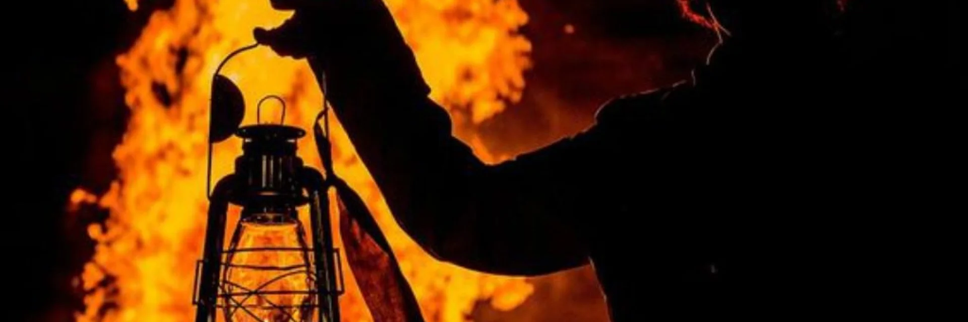 Silhouette tenant une lanterne allumée devant le feu de la Saint-Jean à Perpignan.