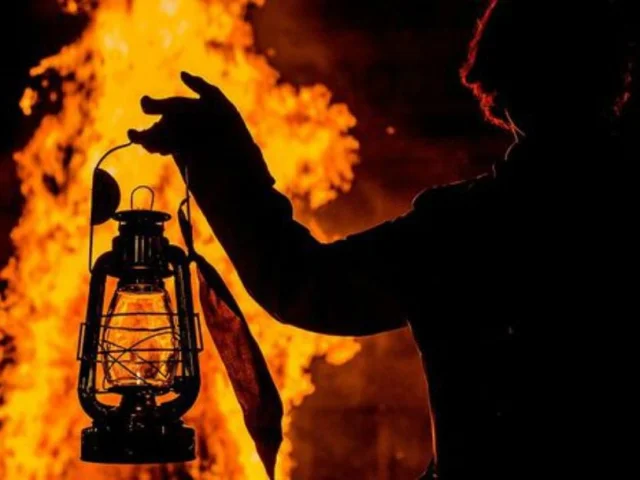 Silhouette tenant une lanterne allumée devant le feu de la Saint-Jean à Perpignan.