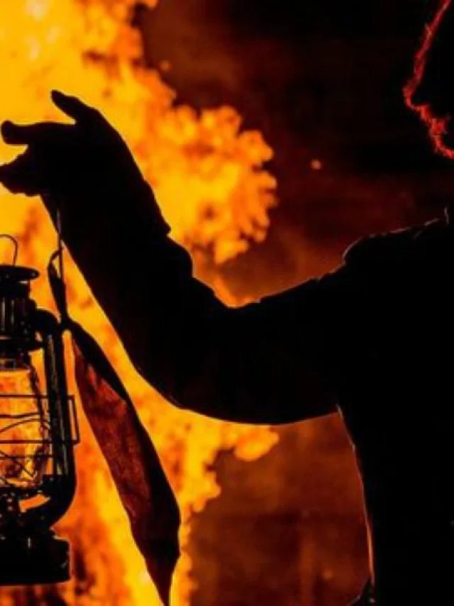 Silhouette tenant une lanterne allumée devant le feu de la Saint-Jean à Perpignan.