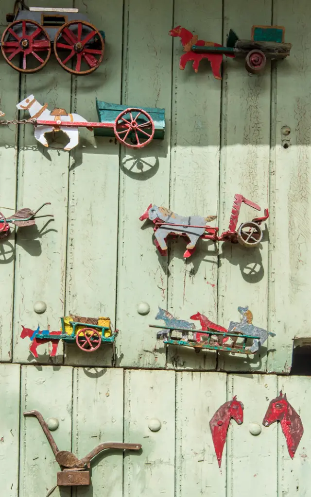 Décor mural original représentant des chevaux et des charrettes miniatures en métal peint, accrochés sur une porte en bois vert pâle.