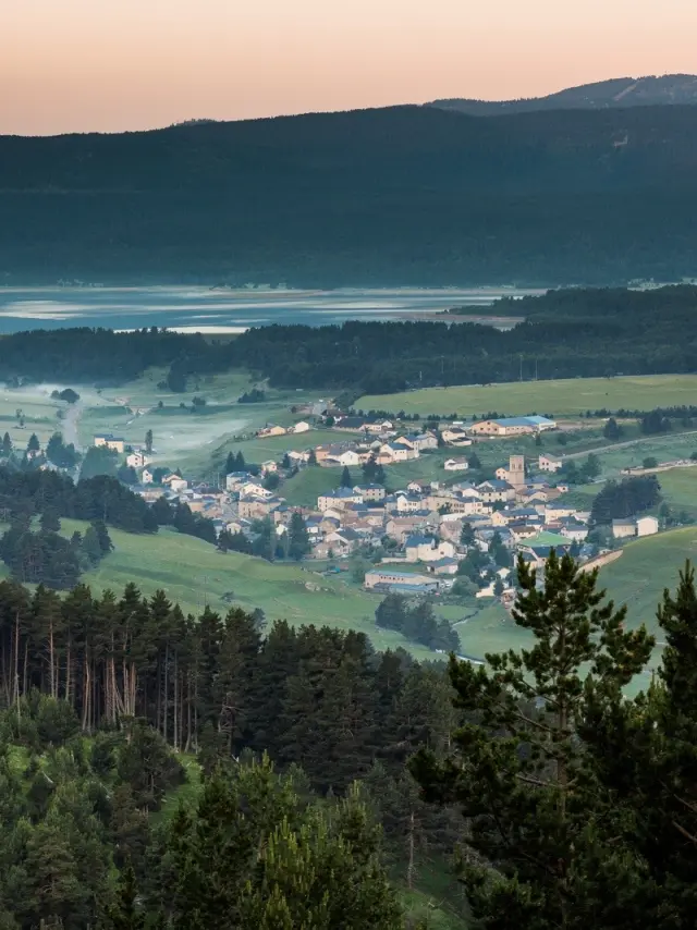 Vue panoramique sur un village de montagne entouré de forêts et de prairies verdoyantes, au lever du jour, dans la région du Capcir.