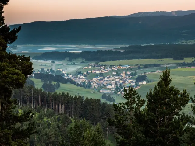 Vue panoramique sur un village de montagne entouré de forêts et de prairies verdoyantes, au lever du jour, dans la région du Capcir.