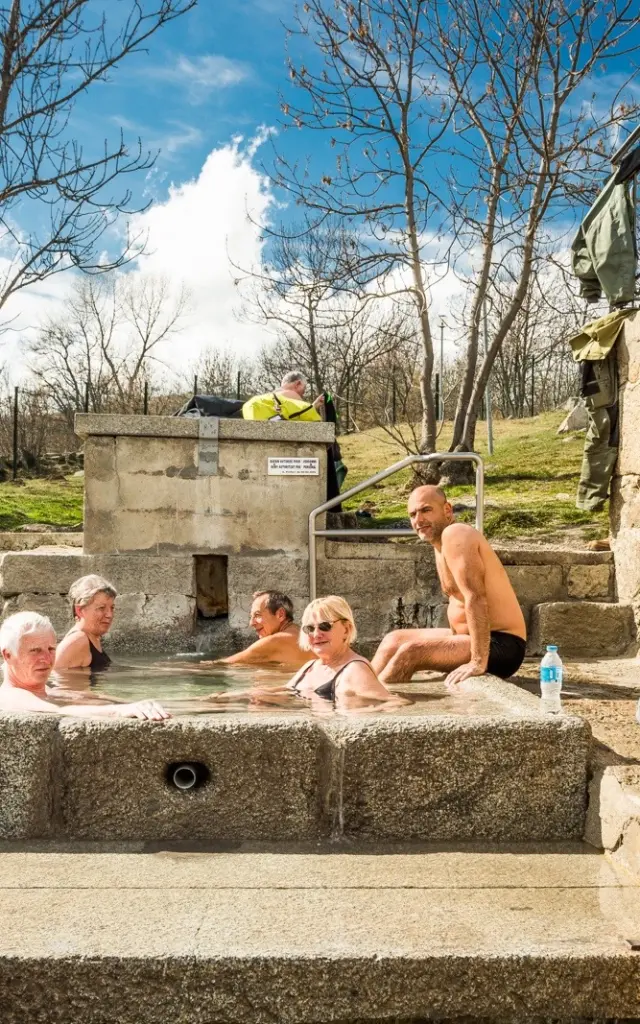 Groupe de personnes se relaxant dans le bassin d’eau chaude naturelle des bains de Dorres, en plein air sous un ciel ensoleillé.