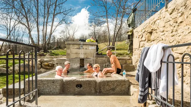 Groupe de personnes se relaxant dans le bassin d’eau chaude naturelle des bains de Dorres, en plein air sous un ciel ensoleillé.