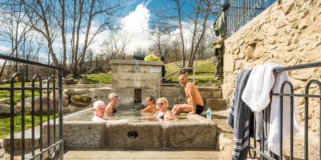 Groupe de personnes se relaxant dans le bassin d’eau chaude naturelle des bains de Dorres, en plein air sous un ciel ensoleillé.