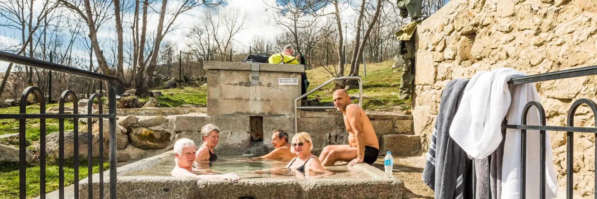 Groupe de personnes se relaxant dans le bassin d’eau chaude naturelle des bains de Dorres, en plein air sous un ciel ensoleillé.
