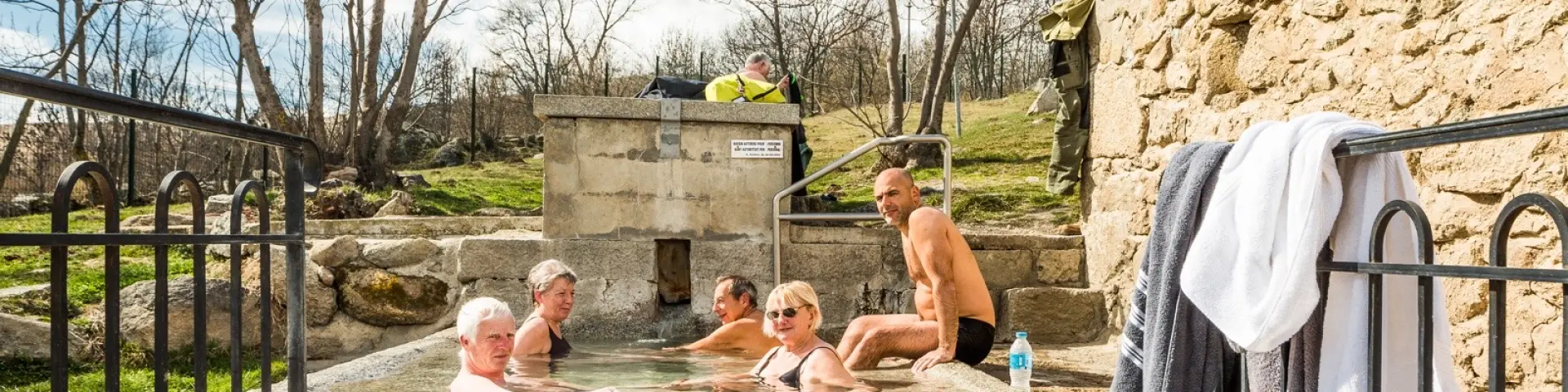 Groupe de personnes se relaxant dans le bassin d’eau chaude naturelle des bains de Dorres, en plein air sous un ciel ensoleillé.