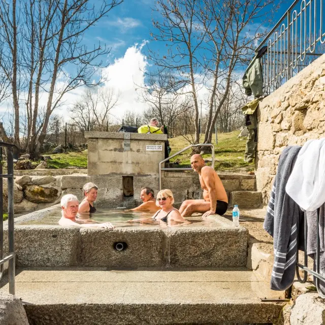Groupe de personnes se relaxant dans le bassin d’eau chaude naturelle des bains de Dorres, en plein air sous un ciel ensoleillé.