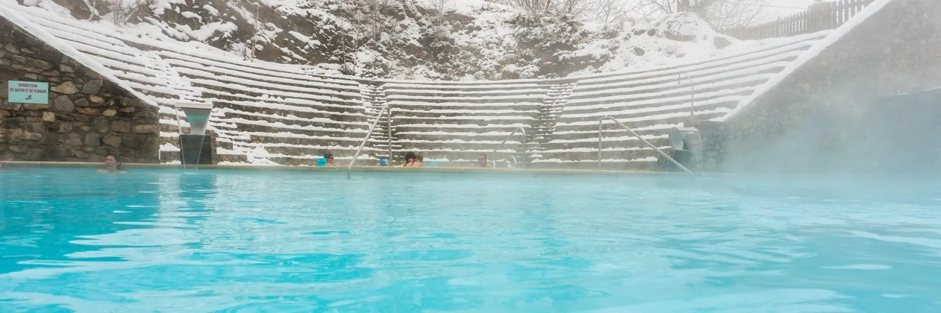 Bassin extérieur des bains de Saint-Thomas-les-Bains entouré de neige, avec des baigneurs profitant des eaux chaudes naturelles en hiver.