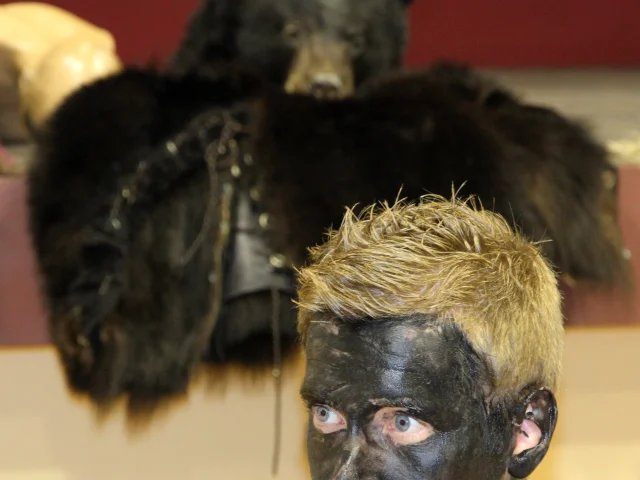 Participant à la Fête de l’Ours, le visage noirci, devant une peau d’ours utilisée pour le costume traditionnel.