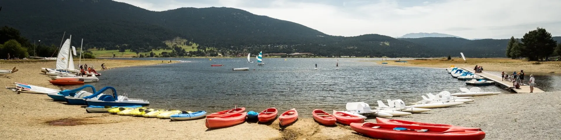Activités nautiques sur la base du lac de Matemale en été, avec kayaks, pédalos et planches à voile au pied des montagnes du Capcir.