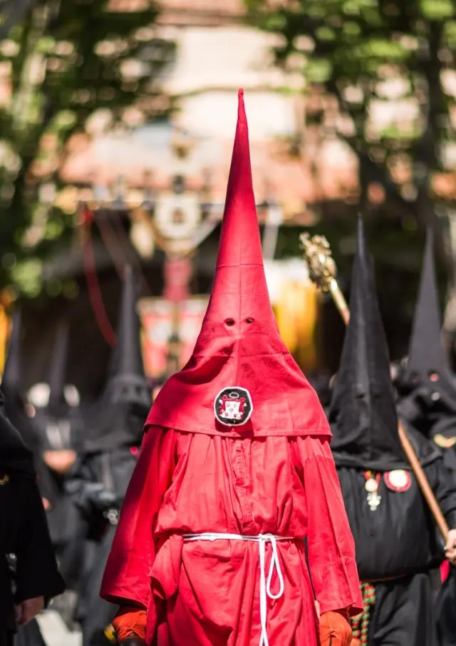 Pénitents vêtus de rouge et de noir défilant dans les rues de Perpignan lors de la Procession de la Sanch, sous le regard du public.