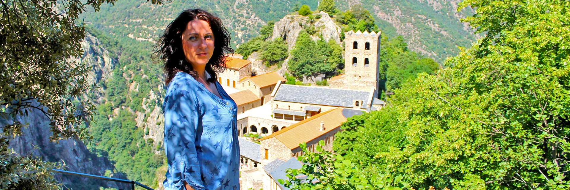 Personne admirant la vue sur l’abbaye Saint-Martin du Canigou, perchée sur son éperon rocheux au cœur des montagnes verdoyantes.